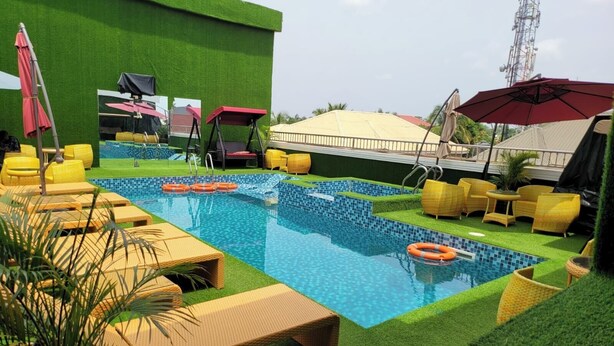A pool area with artificial grass, lounge chairs, and umbrellas. - TOZY  HOTEL (Gwagwalada)