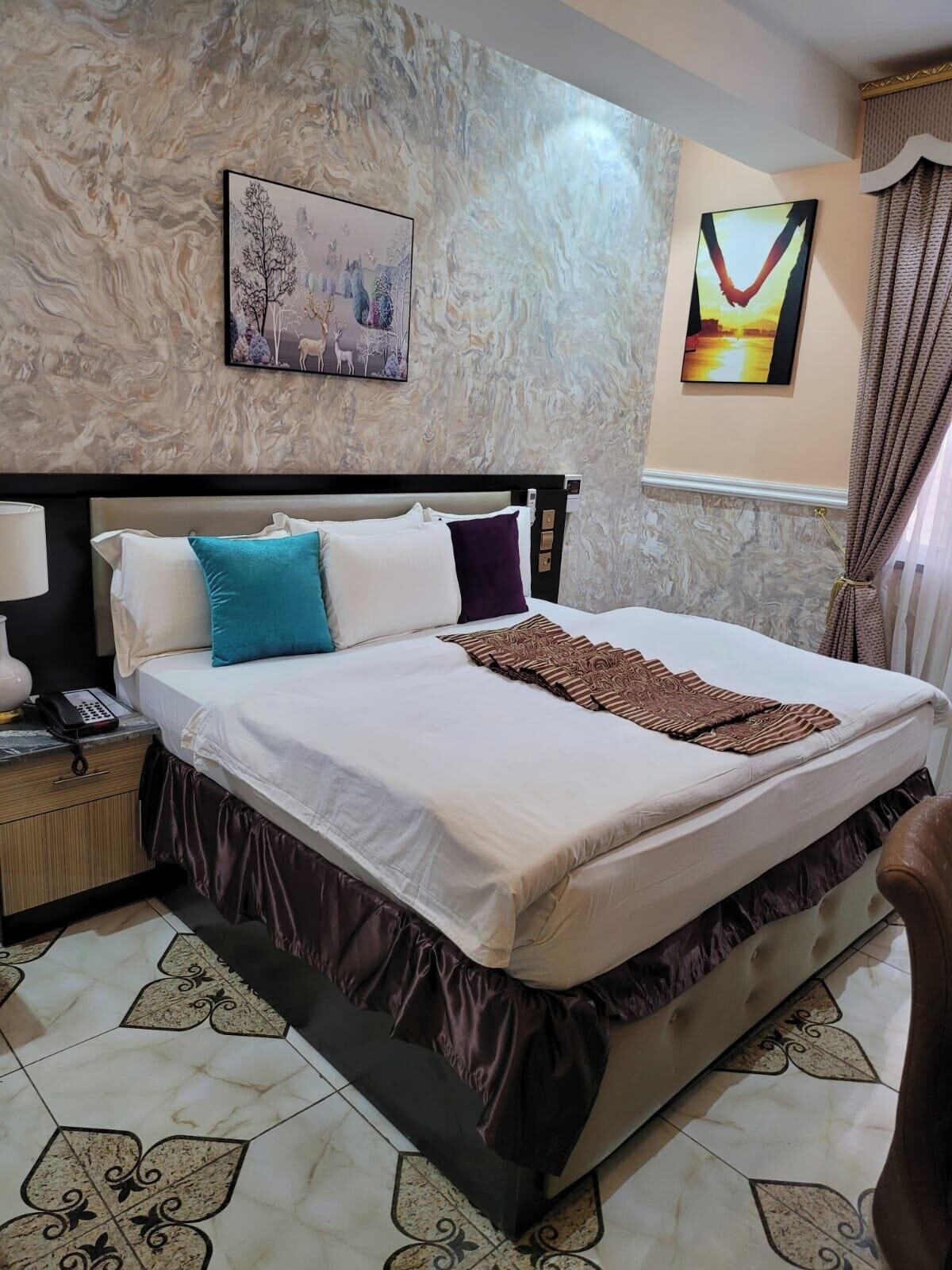 A neatly made bed with a patterned throw, a bedside lamp, and a nightstand with a phone.