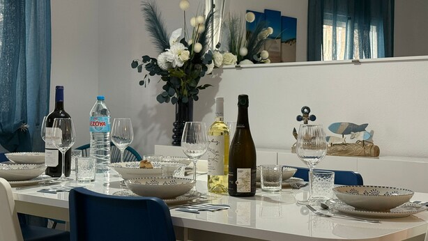A dining table set with plates, bowls, glasses, and bottles, surrounded by chairs.