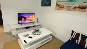 Una sala de estar moderna con un televisor de pantalla plana, una mesa de centro con diversos objetos, un sofá y obras de arte en las paredes.