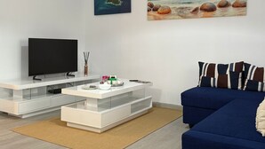 A modern living room with a flat-screen TV, white entertainment unit, and a blue sofa.