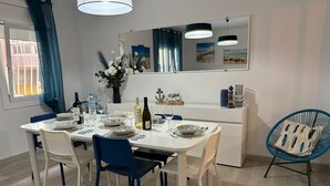 A dining area with a white table set for four, blue chairs, a blue chair with a cushion, a white cabinet, and a mirror above the table.