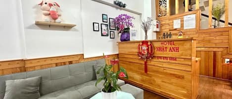 A hotel reception area with a wooden reception desk, a grey sofa, and a small table with a plant.