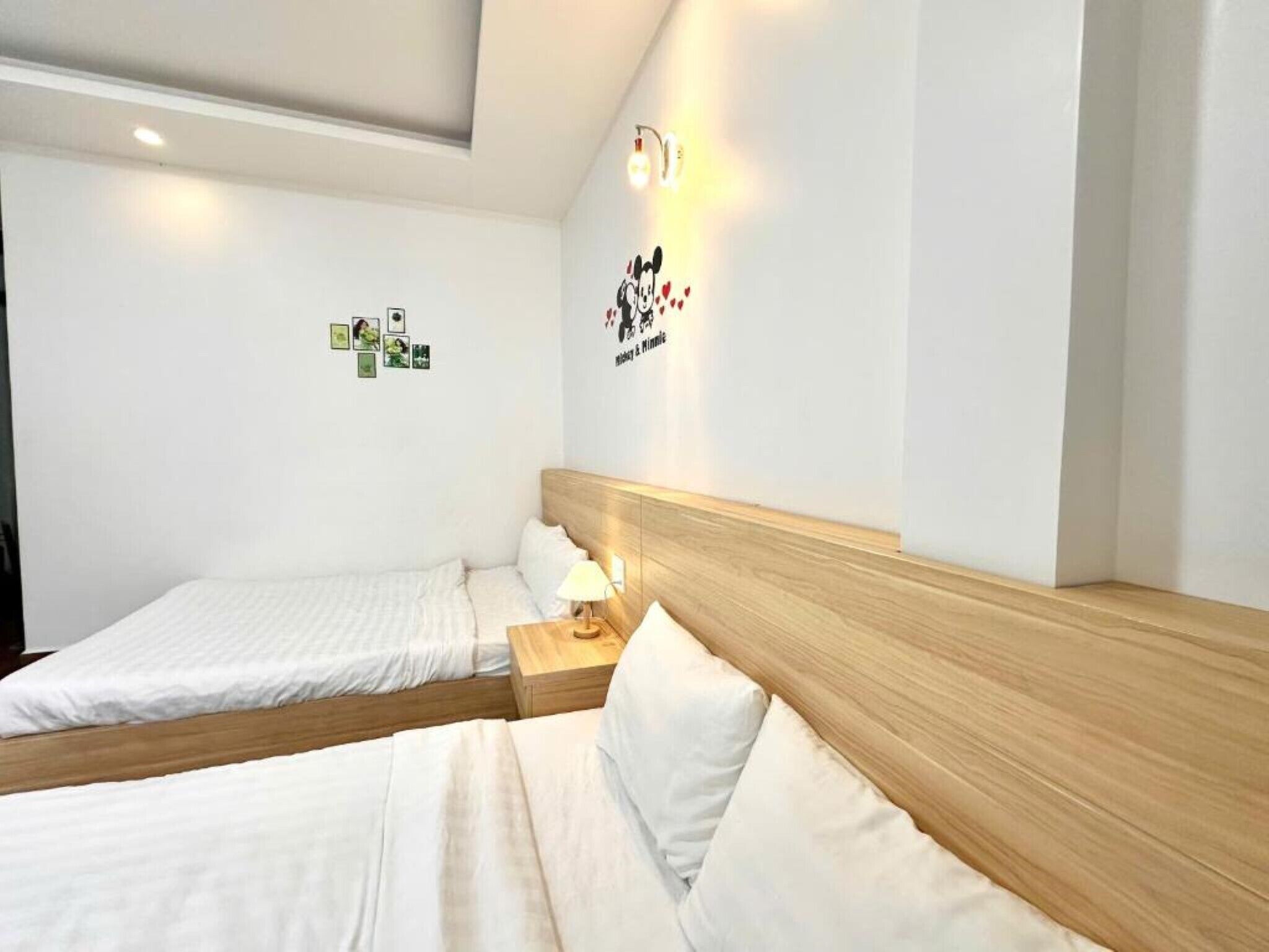 Une chambre d’hôtel avec deux lits simples, une tête de lit en bois, une table de chevet avec une lampe et des éléments de décoration murale, notamment une citation et des photos.