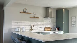 Een moderne keuken met een groot eiland, barkrukken, een roestvrijstalen afzuigkap en een betegelde achterwand.