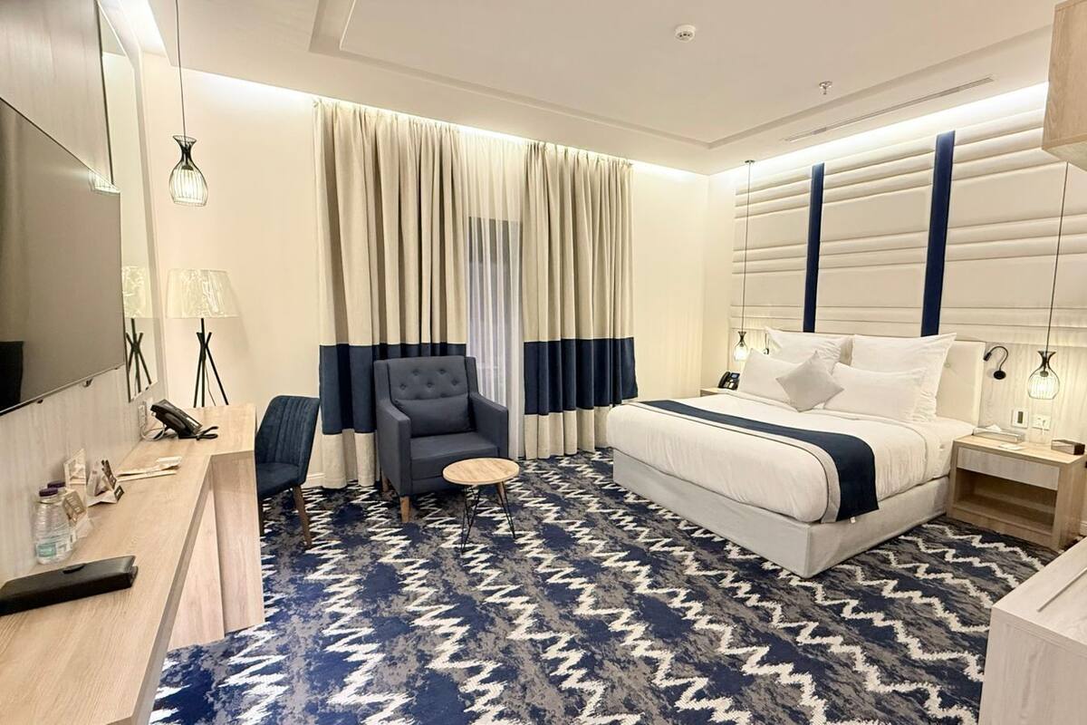 A modern hotel room with a large bed, a desk, a chair, and a television.