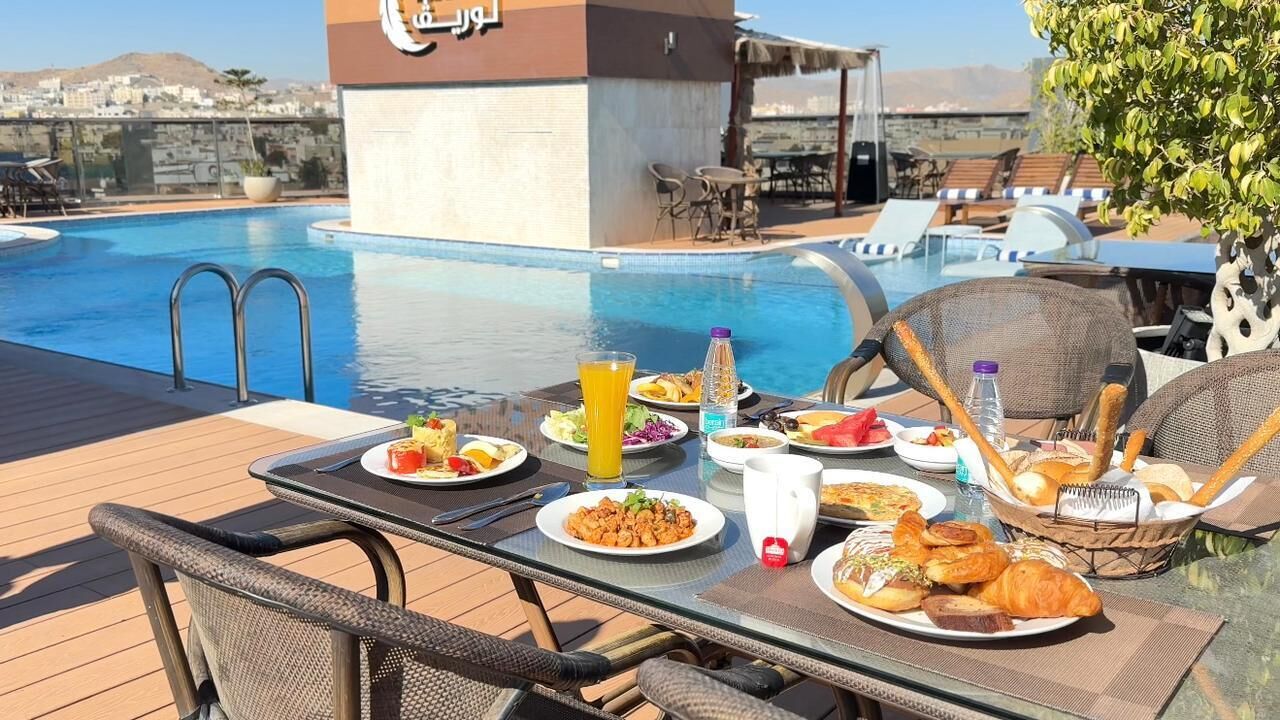 Una mesa de comedor con alimentos para el desayuno y una piscina al fondo.