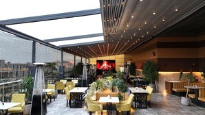 A rooftop restaurant with glass walls, yellow chairs, and a central seating area with a fire feature. - Le Reve Hotel (Taif)