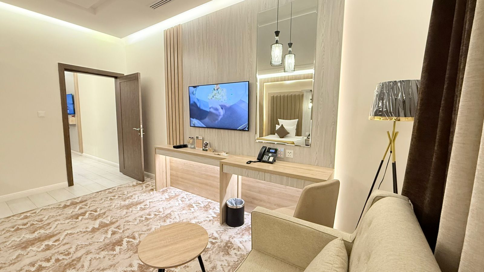 A modern hotel room with a wooden desk, a flat-screen TV, a sofa, and a small round table.