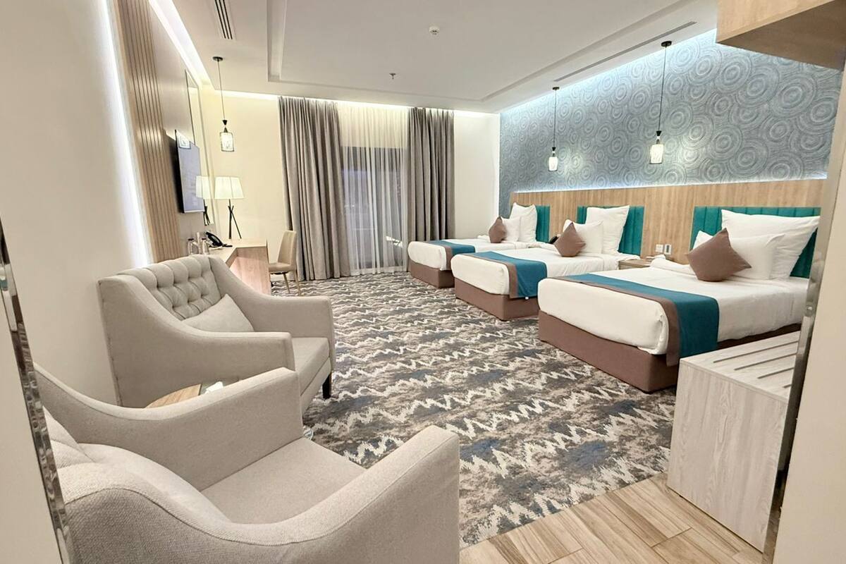 A hotel room with a large bed, two smaller beds, a sofa, a desk, and a patterned carpet.