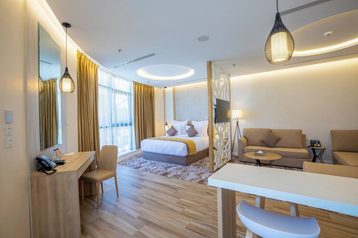 A modern hotel room with a bed, a desk, a sofa, and a dining area.