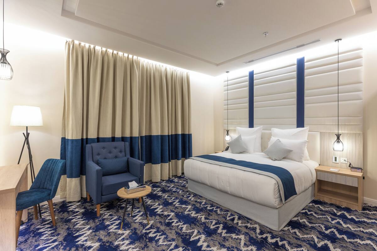 A hotel room with a bed, a desk, a chair, and a lamp.