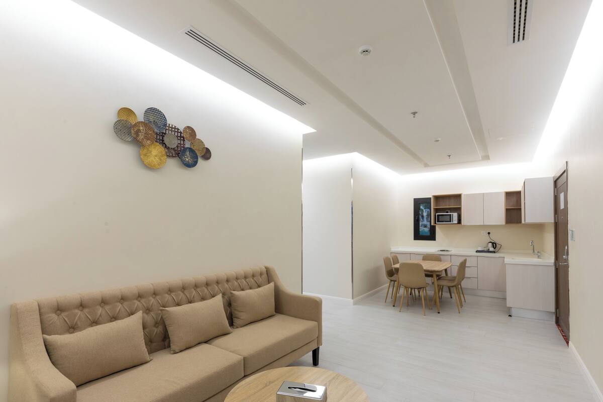 A modern living room with a beige sofa, a coffee table, and a dining area with chairs and a table.