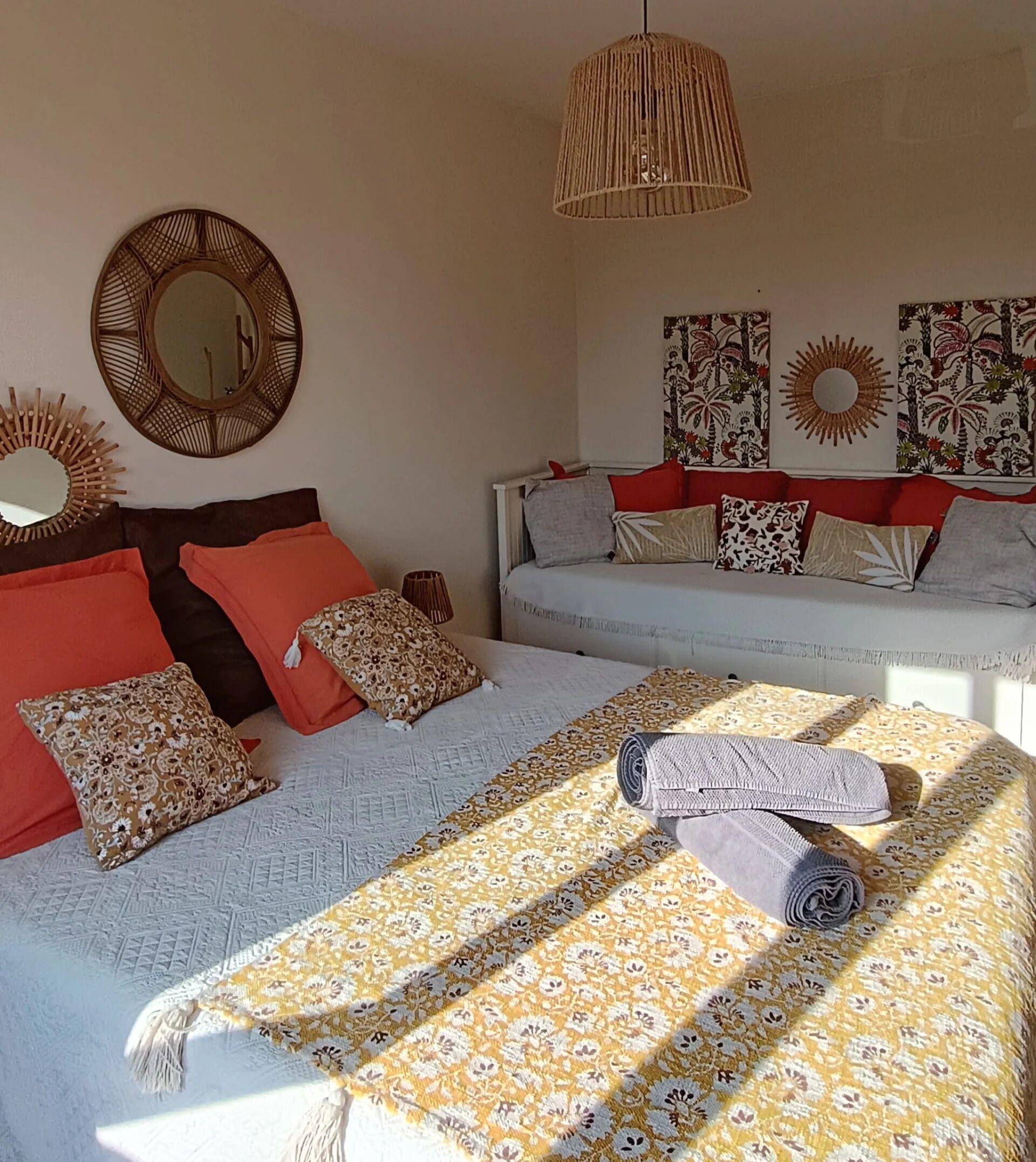 Een slaapkamer met een bed, kussens, een hanglamp en wanddecoratie.