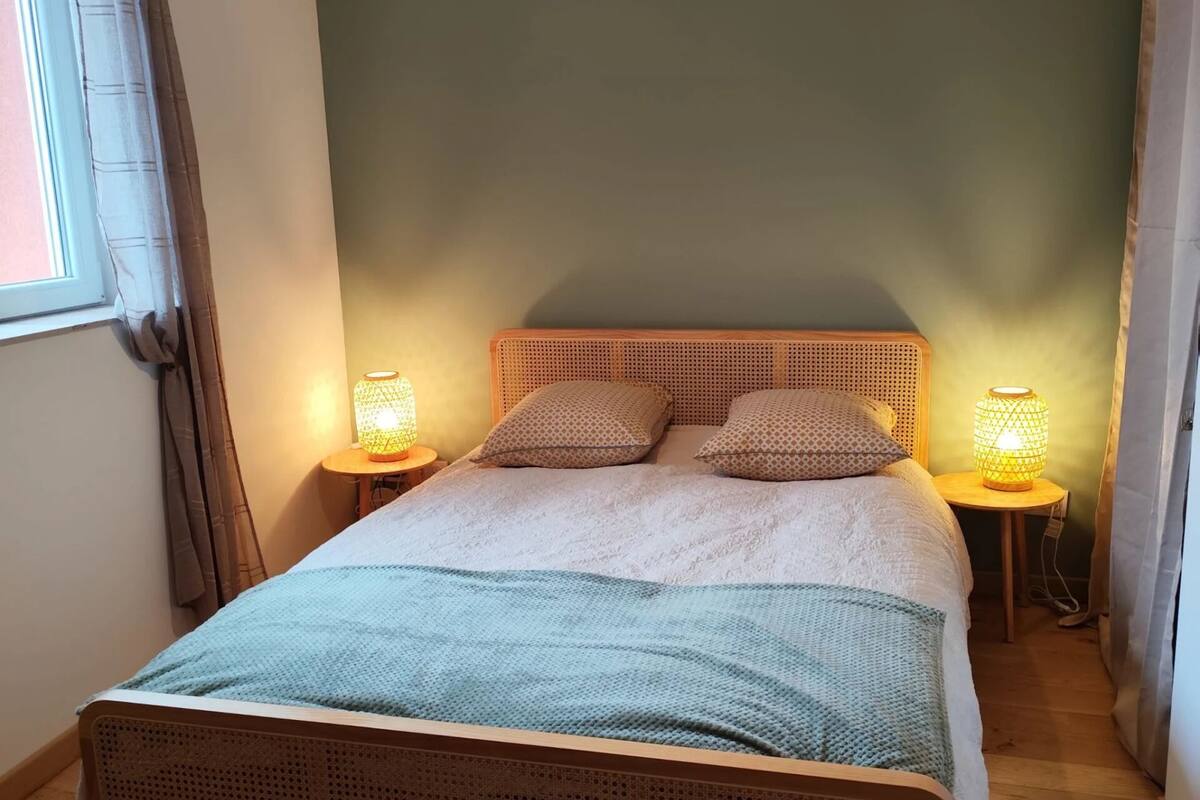Ein Schlafzimmer mit einem Bett, zwei Nachttischlampen, einer Pendelleuchte und einem Fenster mit Vorhängen.