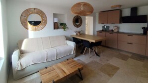 A modern living room with a sofa, a wooden coffee table, and a dining area with a table and chairs. There is a kitchen area with cabinets and a TV mounted above the counter. - La grange aux fées Amnéville (Amnéville)
