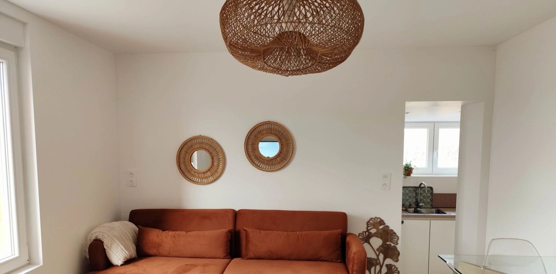 A living room with a brown sofa, two wall-mounted mirrors, and a woven ceiling light fixture.