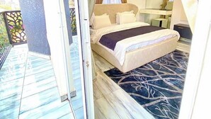 Une chambre à coucher avec un lit, une table de chevet et un miroir. Il y a un balcon avec une balustrade et une vue sur l’extérieur.