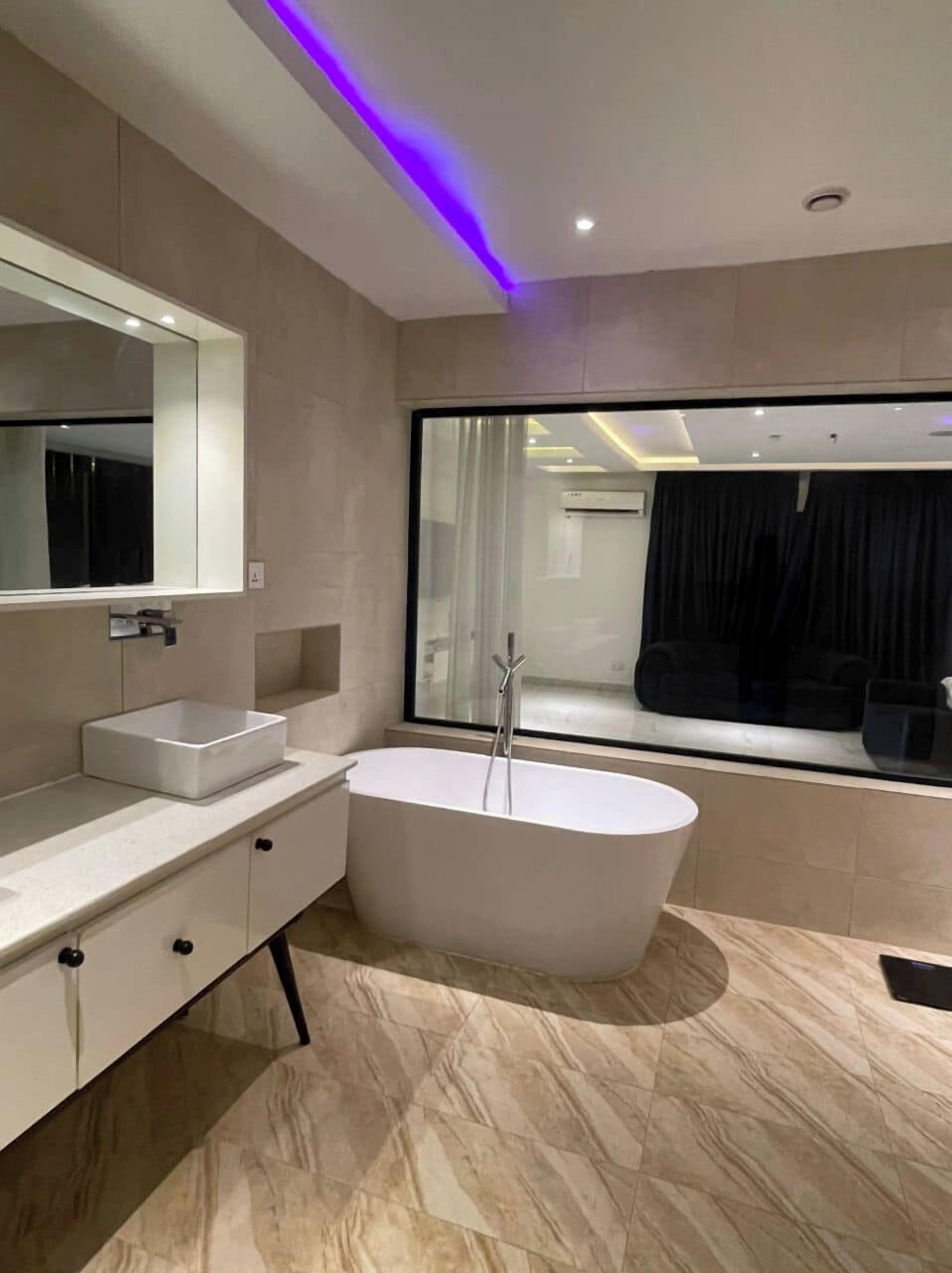 Un baño moderno con una bañera independiente, un espejo grande y una ventana con cortinas.