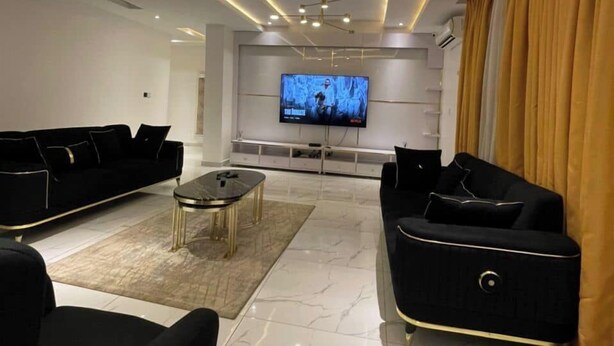 Un salon moderne doté d’un téléviseur à écran plat, de canapés noirs et d’un sol en marbre.
