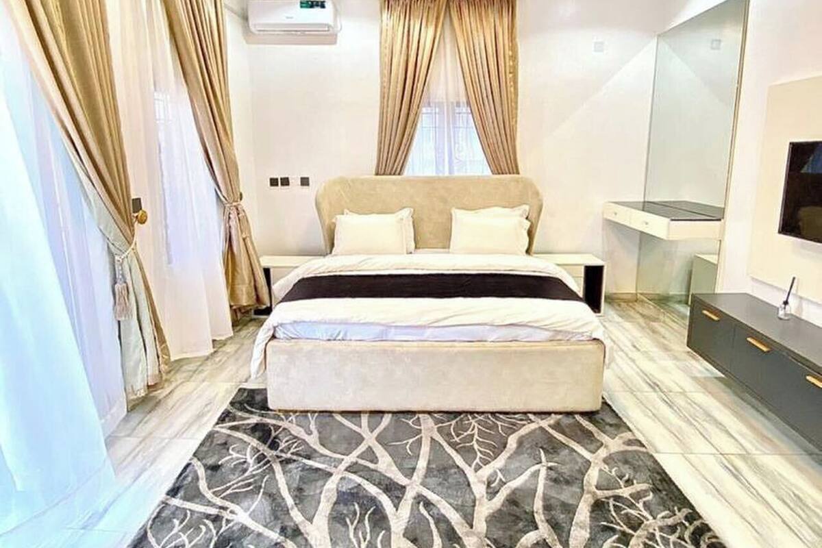 Ein Schlafzimmer mit einem Bett, einem großen Spiegel, einer Kommode und einem gemusterten Teppich.