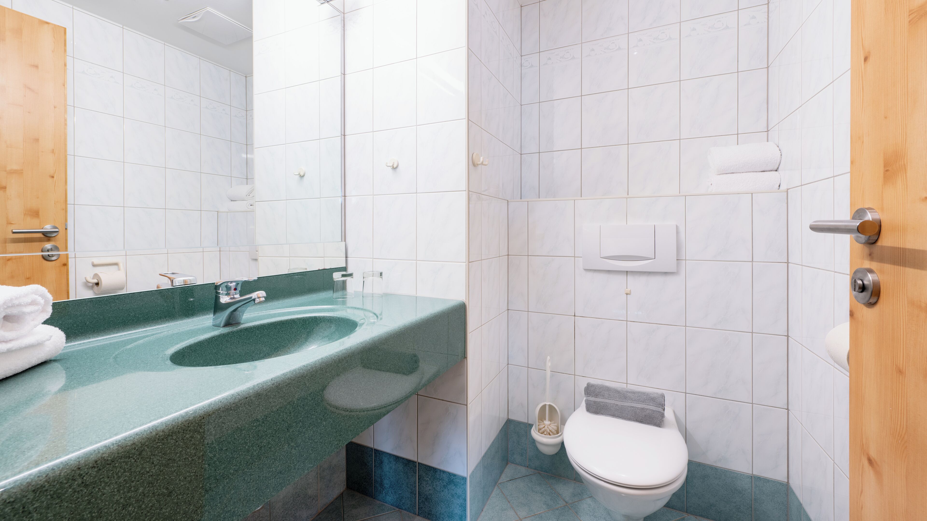 A bathroom with a green sink, white toilet, and a wooden door.