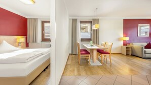 A hotel room with a bed, a dining table with chairs, a sofa, and a window with curtains. - Hapimag Saalbach (Saalbach)