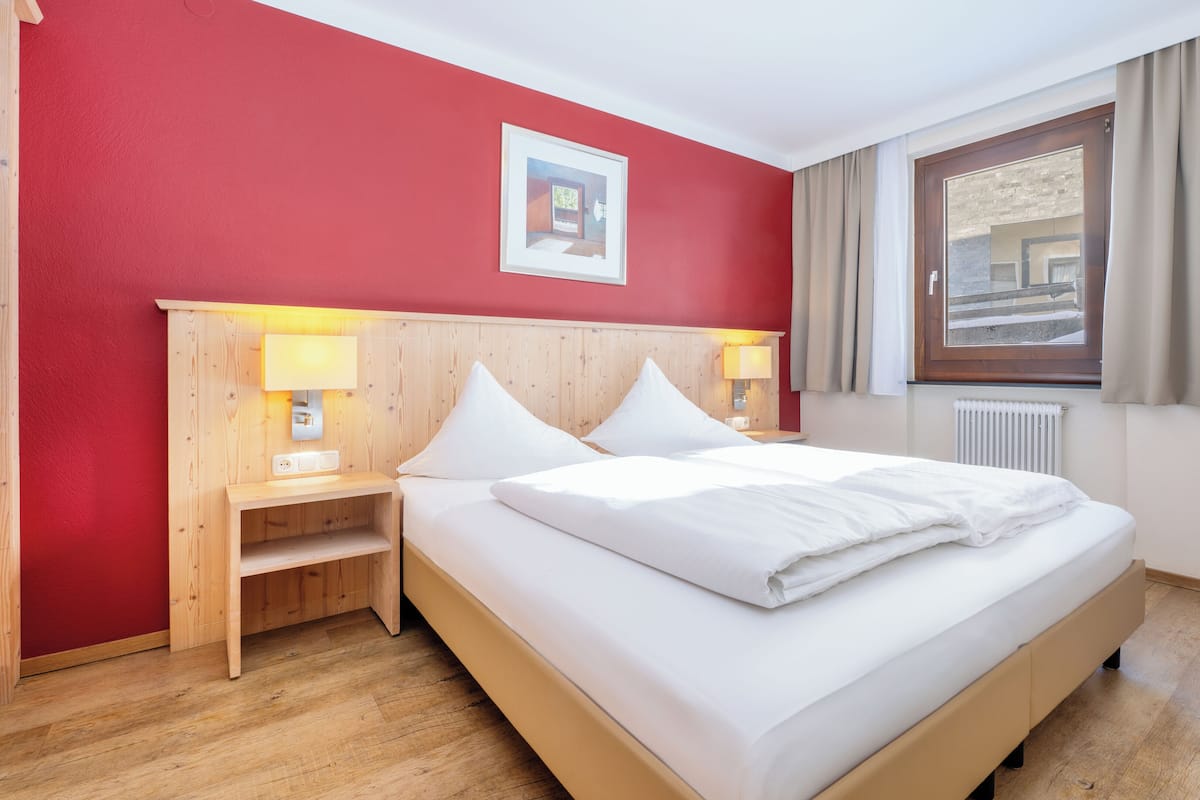 Una habitación de hotel con una cama de madera, paredes rojas y una ventana con cortinas.