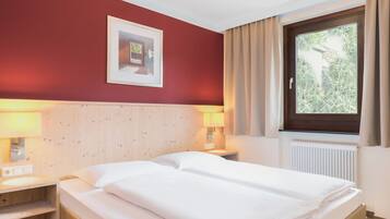 A hotel room with a wooden headboard, two bedside lamps, a window with curtains, and a framed picture on the wall.