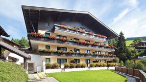 A multi-story hotel with balconies adorned with flowers, a well-maintained lawn, and a clear sky. - Hapimag Saalbach (Saalbach)