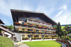 Un hotel de varios pisos con balcones decorados con flores, un césped cuidado y un cielo despejado.