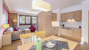 A modern hotel room with a wooden dining table, a sofa, a red armchair, and a kitchen area with wooden cabinets and a stove. - Hapimag Saalbach (Saalbach)