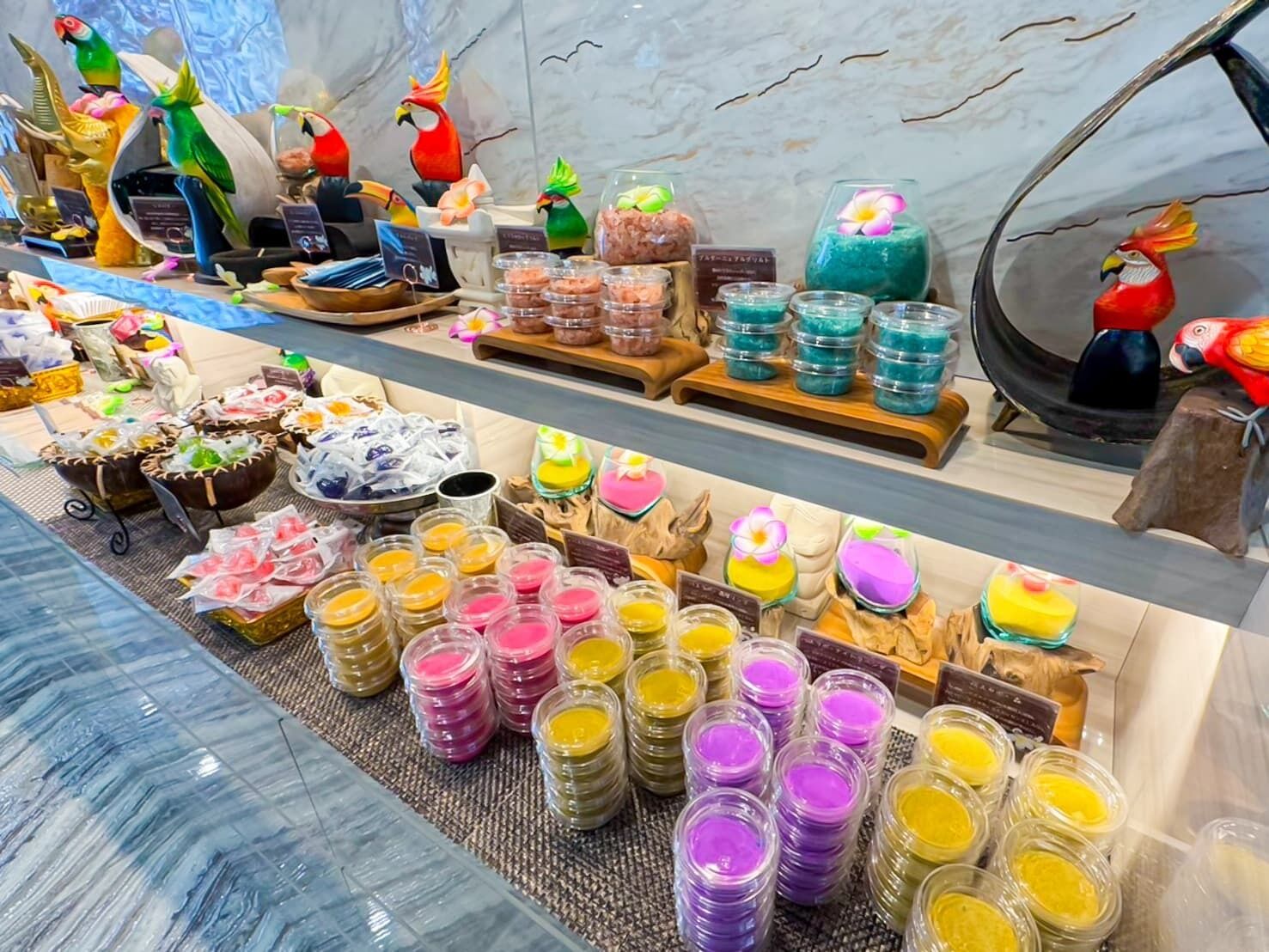A variety of colorful packaged goods displayed on shelves and tables, with decorative bird figures and a marble wall in the background.