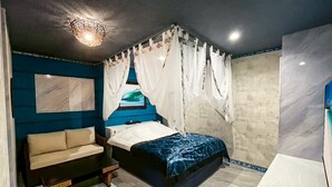 Une chambre à coucher comprenant un lit, un canapé, un luminaire au plafond et un téléviseur fixé au mur.