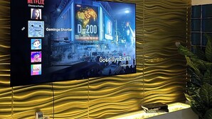 A flat-screen TV mounted on a wall with a textured golden design. - Safe Court Apartment (Lekki)