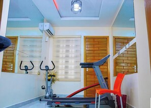 A gym with exercise equipment, a ceiling fan, and a window with blinds. - Safe Court Apartment (Lekki)
