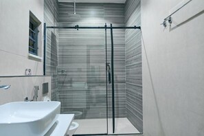 A modern bathroom with a glass shower enclosure, a white sink, and a toilet. - Safe Court Apartment (Lekki)