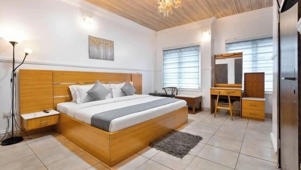 A modern bedroom with a wooden bed, bedside tables, a desk, and a wardrobe. - Safe Court Apartment (Lekki)