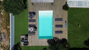 An aerial view of a rectangular swimming pool surrounded by a wooden deck with multiple lounge chairs and umbrellas. - Villa with pool in Lecci (Lecci)