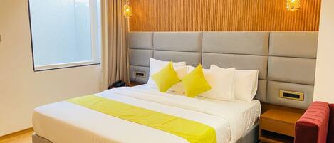 A hotel room with a large bed, a wooden headboard, a bedside table, a red armchair, and a window with curtains.