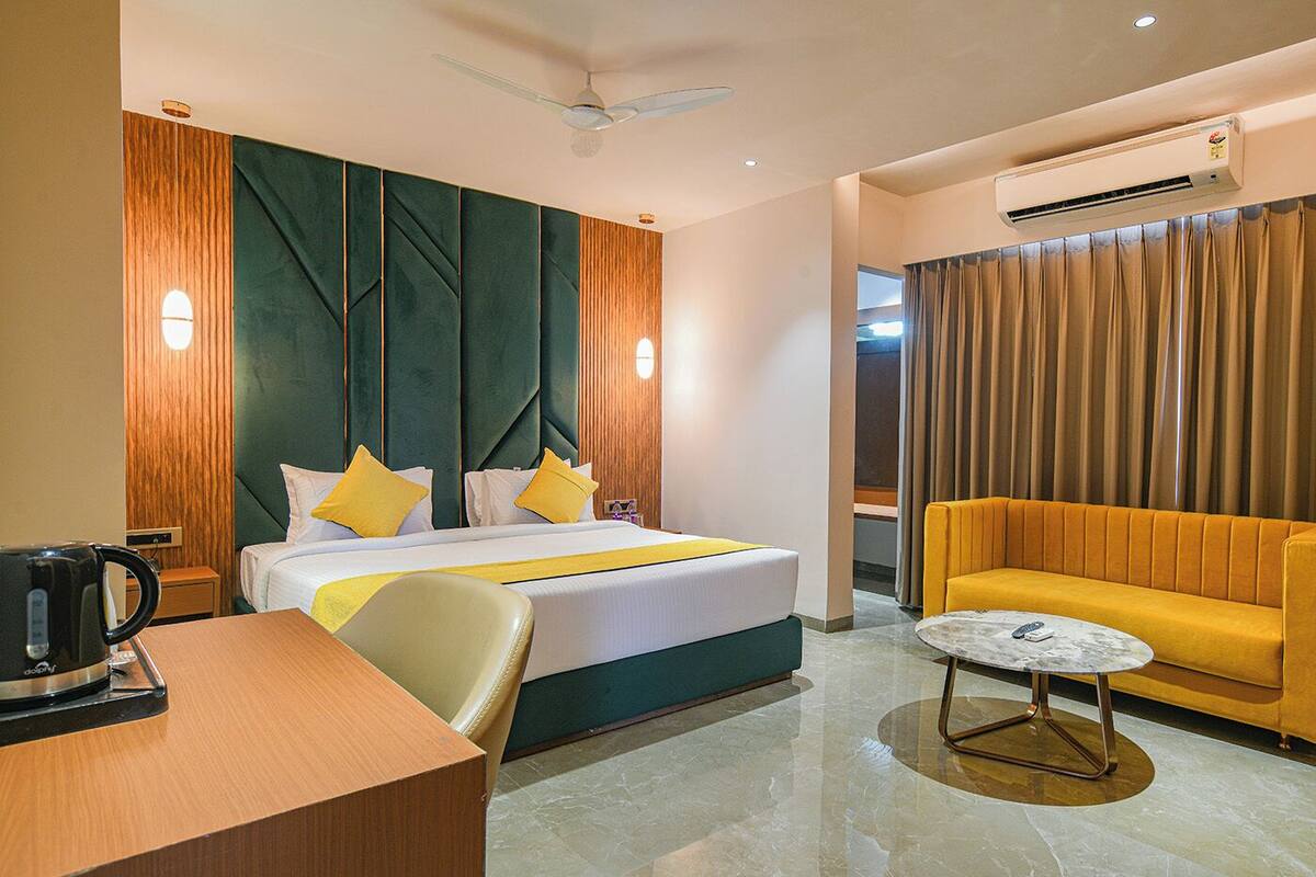 A hotel room with a bed, a sofa, a coffee table, a desk, and an air conditioning unit.