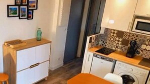 A compact kitchen with a microwave, dishwasher, and a small dining area with a wooden table and stools. - Charming t2 with loggia, beautiful sea view + parking lot (Saint Pierre La Mer)
