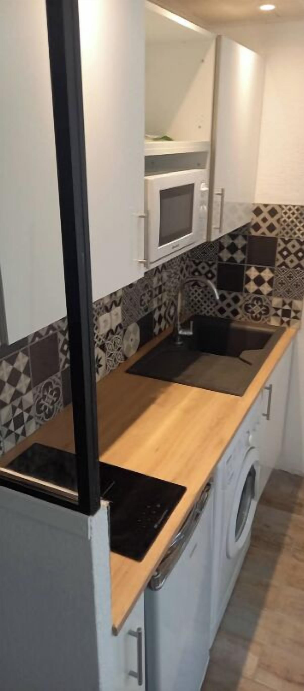 Ett kompakt kök med mikrovågsugn, diskho och tvättmaskin.