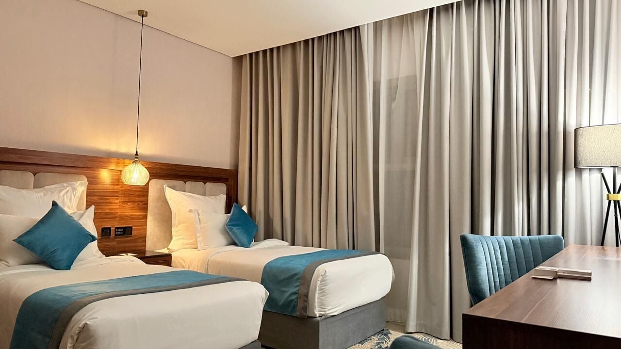 Une chambre d’hôtel avec deux lits, une tête de lit en bois, une table à manger et une lampe.