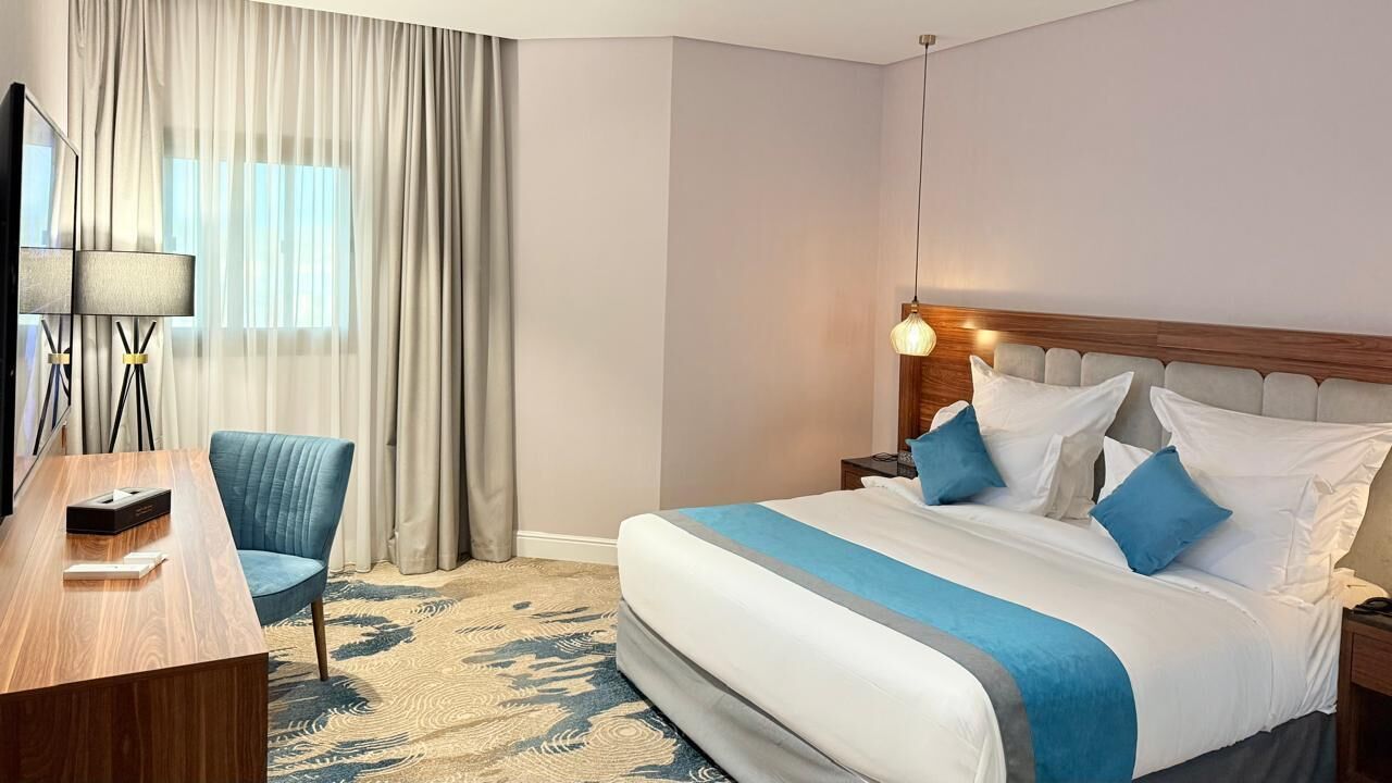 A hotel room with a large bed, a desk, a chair, and a lamp.