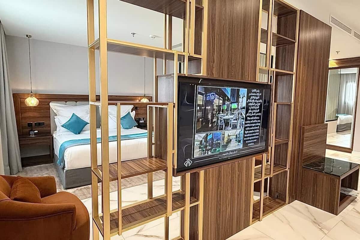 A hotel room with a bed, a TV, a sofa, and a wooden partition.