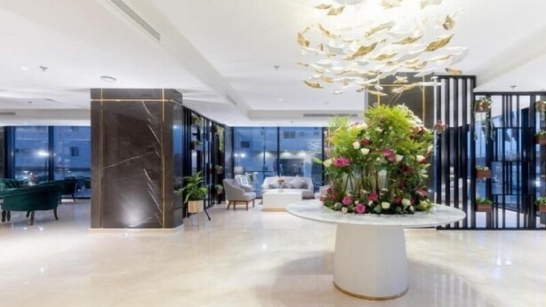 En moderne hotellobby med en marmorsøjle, en blomsterdekoration centralt placeret og et siddeområde med en sofa og stole.