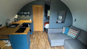 A compact living space with a kitchen, a sofa, and a dining area. - Pea Pod Self-Catering glamping in Suffolk (Henley)