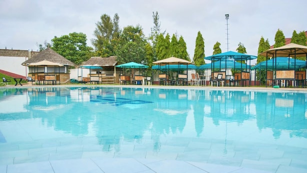 A swimming pool with lounge chairs and umbrellas, surrounded by trees and buildings. - Cedar (Athi River)
