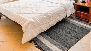 A neatly made bed with white bedding, a wooden headboard, a bedside table with a lamp, and a decorative hanging light fixture. - Cedar (Athi River)